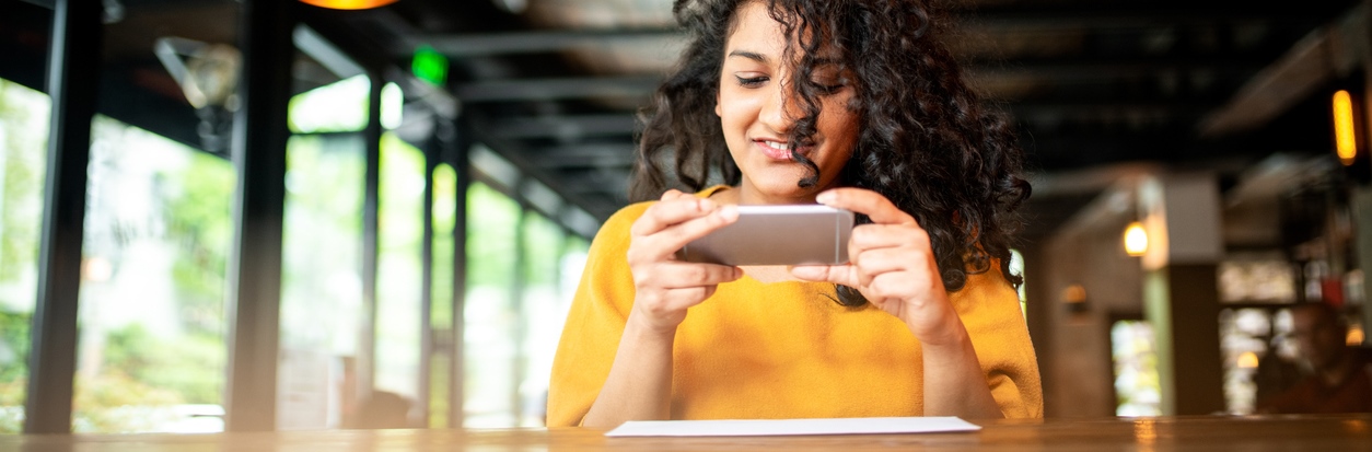 Woman in yellow shirt depositing a check by her phone using remote deposit capture.