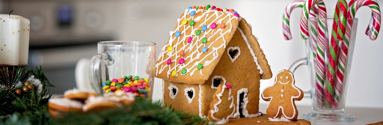 Gingerbread house decorated next to a gingerbread man and a glass of candy canes.