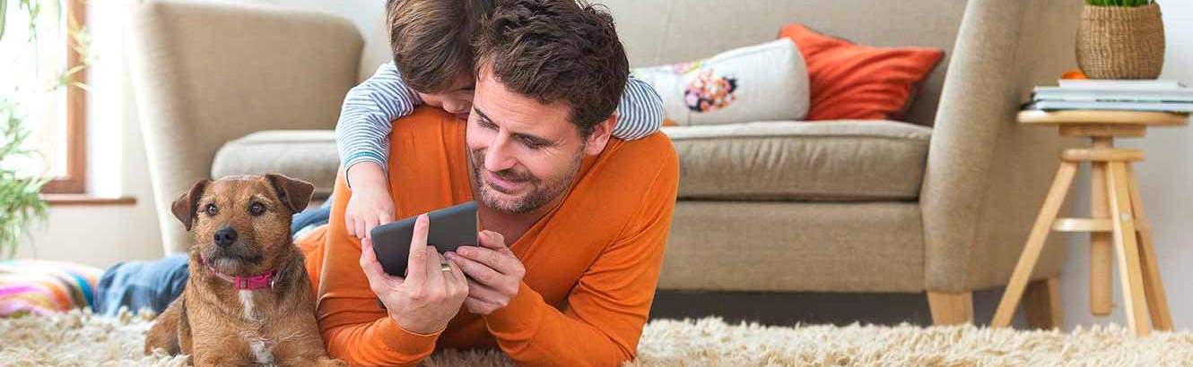 Father, son and dog lying on the floor and looking at a phone.