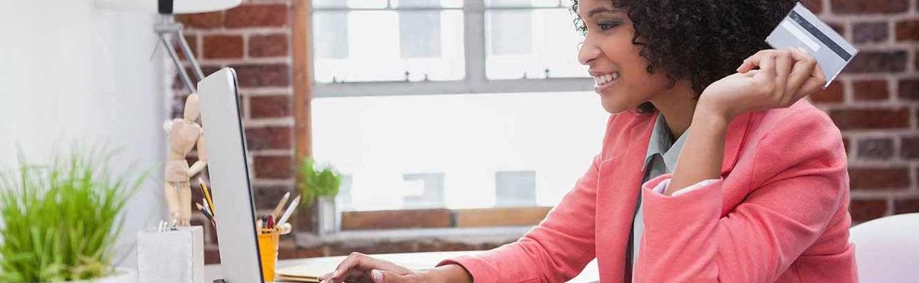 Person looking at the computer screen with a credit or debit card in her hand to make an online purchase with a card from Pilot Grove Savings Bank