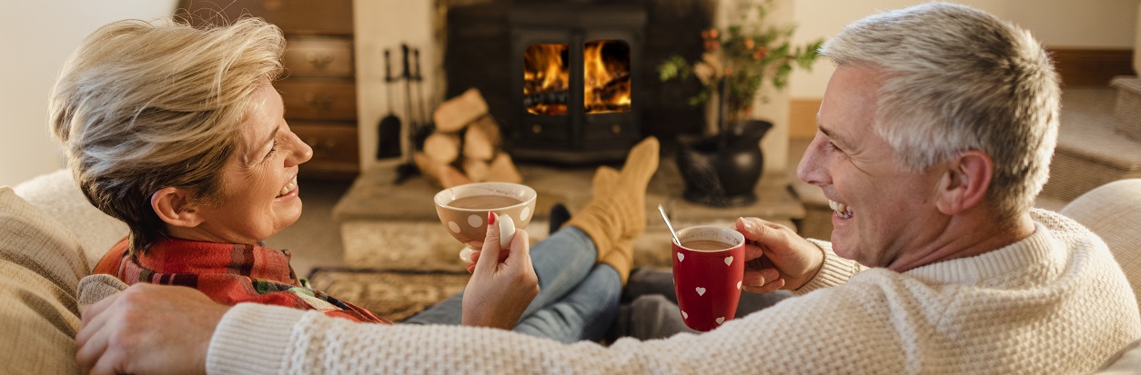 Couple sitting on the couch by the fire sipping hot cocoa.