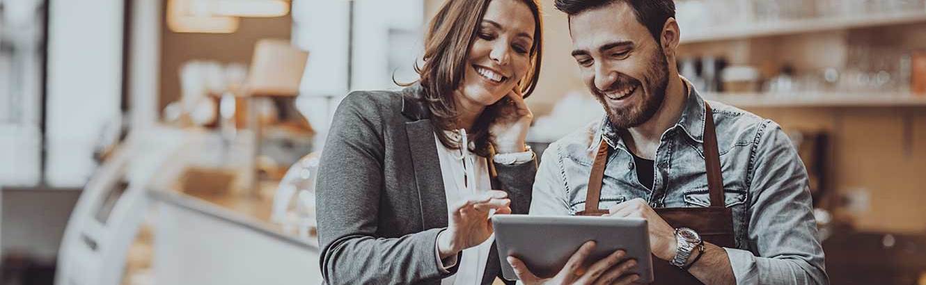 Two people look at a tablet screen in a coffee shop after getting a small business loan with Pilot Grove Savings Bank